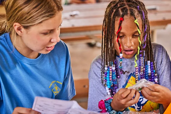 Two Cub Scouts work on a craft project together, one reading the instructions while the other opens the materials.