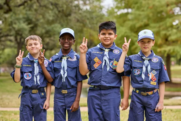 Four Cub Scouts in blue uniforms giving the Cub Scout sign outdoors.